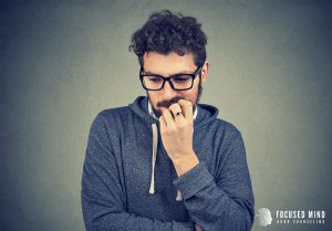 Man with glasses bites his nails with a nervous look on his face. He is experiencing emotional dysregulation as a result of his adult adhd. Focus Mind ADHD Counseling offers ADHD therapy for adults in Columbus, Ohio, ADHD emotional regulation, and more. Contact us today for adult ADHD therapy today.