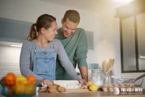 Man with ADHD stands next to his wife in the kitchen. She is rolling out dough for baking, and he feels happy thanks to emotional regulation therapy in Columbus, OH. Focus Mind ADHD Counseling offers ADHD emotional regulation, ADHD treatment for adults, and more. Contact us today for supprt! 
