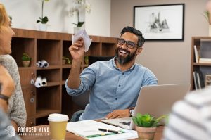 A man prepares to throw a paper airplane to their co-worker as they smile. This could represent the positive outcome of working with a therapist in Columbus Ohio for ADHD and emotional regulation. Focused Mind ADHD Counseling can offer online therapy in Columbus, OH today. 43235 | 43202 | 43214