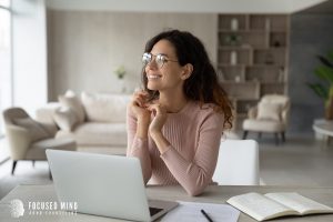 A woman sitting in front of a laptop and open book smiles as she looks out the window. Focused Mind ADHD Counseling can offer support with adult ADHD treatment in Columbus, OH. Learn more about our services by contacting an adult ADHD specialist in Ohio today! 43235 | 43220 | 43035