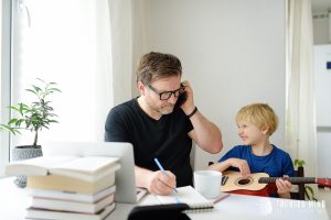 A father eyes their loud son as they take notes while on the phone. This could represent the distraction working from home with ADHD in Columbus, OH can cause. Contact an adult ADHD therapist in Ohio to learn more about ADHD working from home in Columbus, OH. 