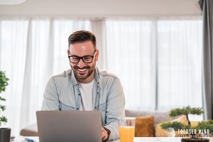 A man smiles as he types on a laptop with orange juice nearby. An adult ADHD therapist in Ohio at Focused Mind ADHD Counseling can offer support with working from home with ADHD in Columbus, OH. Contact a therapist in Columbus Ohio to learn more! 