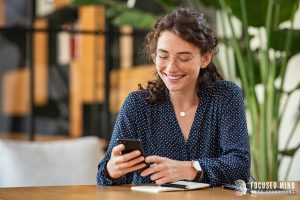 A woman smiles while looking at her phone. This could represent finding the right therapist in Columbus Ohio. Learn more about online therapy in Columbus, Ohio by searching "ADHD therapist for adults near me" today. Focused Mind ADHD Counseling would be happy to support you!