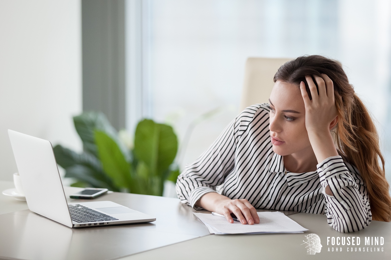 A woman sits with a hand against her head while looking at her laptop. ADHD testing in Columbus, OH can help you come to terms with adult ADHD. Learn more about ADHD and emotional regulation with Focused Mind ADHD Counseling to learn more.