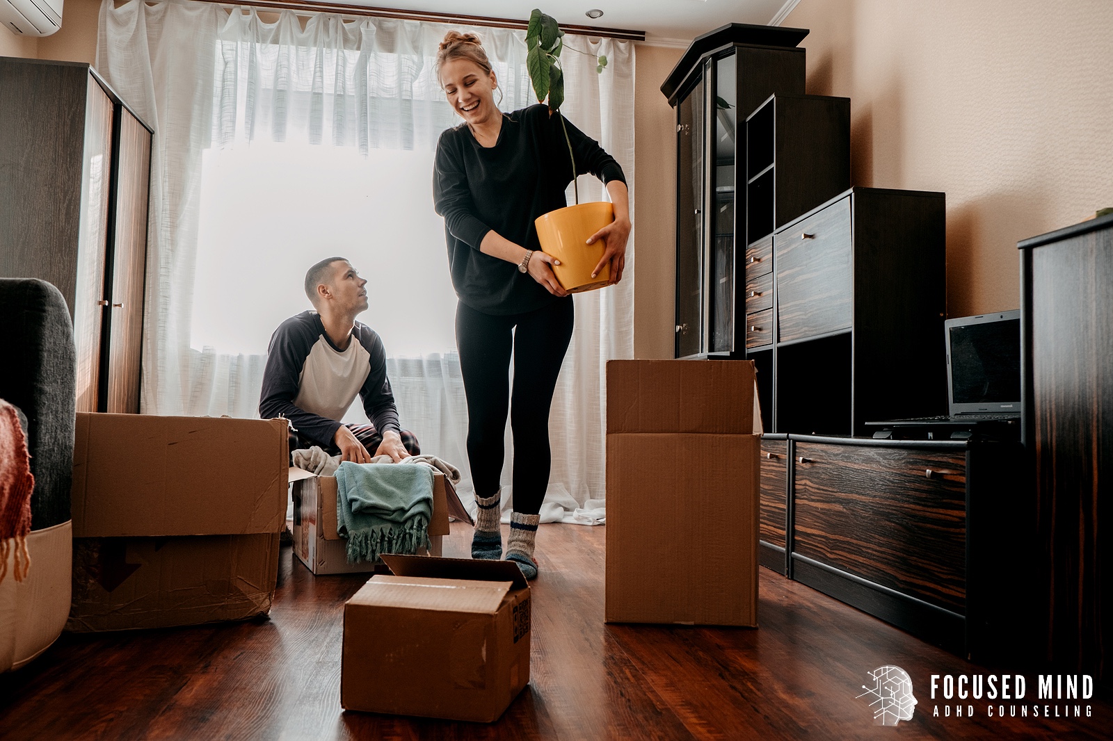 A woman holds a bucket while walking around moving boxes. Focused Mind ADHD Counseling can offer support for life transitions and ADHD and emotional regulation. Learn more by searching ADHD therapist for adults near me.