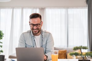 A man smiles while typing on his laptop. This could represent the joy of finding clarity of ADHD symptoms. Learn more about Focused Mind ADHD Counseling by searching "what are anxiety symptoms Columbus, OH" or emotional regulation therapy in Columbus, OH today.