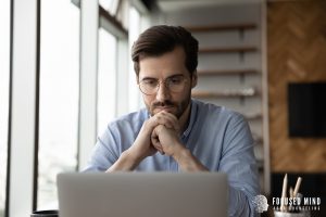 A man sits in front of his laptop with a pensive look. This could represent the search for understanding ADHD symptoms Ohio. Learn more about this and anxiety symptoms Columbus, Oh by searching "what are anxiety symptoms Columbus, OH" today.