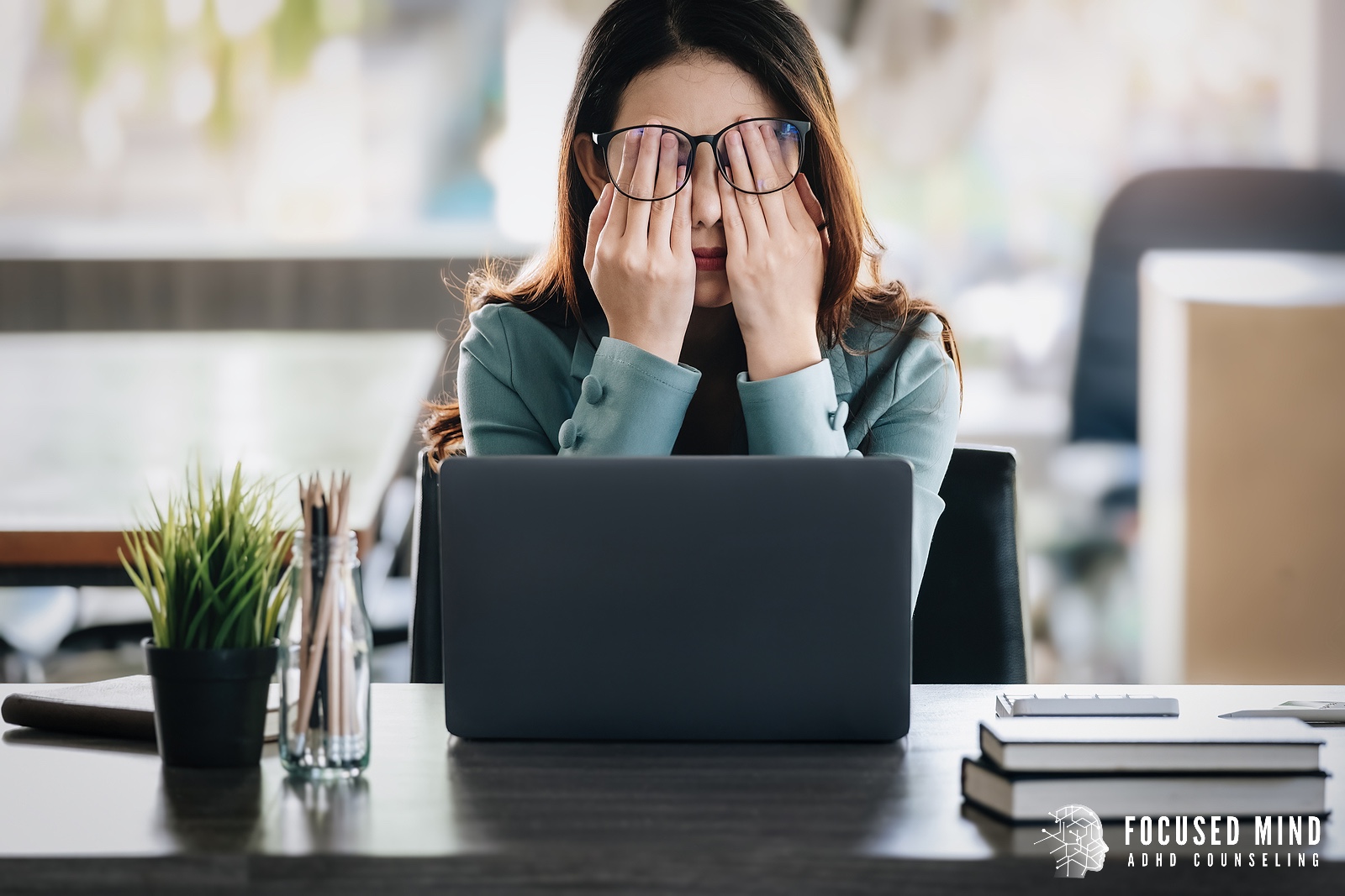 A woman covers her face while sitting at a laptop desk. Online ADHD treatment in Columbus, OH can help you cope with ADHD thought loops and more. Contact a therapist in Columbus Ohio for support today.