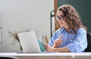 A woman smiles while gesturing and talking to her laptop. This could represent overcoming work overwhelm with the help of a therapist in Columbus Ohio. Learn more about the support online therapy in Columbus, OH can offer by searching “adhd therapist for adults near me” today.