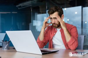 A man touches his temples with a stressed expression while looking at his laptop. Learn more about ADHD treatment for adults in Ohio and emotional regulation therapy in Columbus, OH today by contacting a therapist in Columbus Ohio. They can offer ADHD productivity hacks and more! 