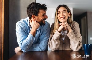A smiling couple sit together at a table, representing the bonds cultiavted when seeking support for ADHD and relationships. Contact an ADHD psychologist in Columbus, OH to learn more about ADHD and emotional regulation. 