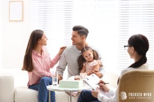 A couple holds their child while sitting across from a woman taking notes on a clipboard. Learn more about the benefits of ADHD testing in Columbus, OH by contacting an adult ADHD specialist in Columbus, OH, or searching for an ADHD specialist near me. 