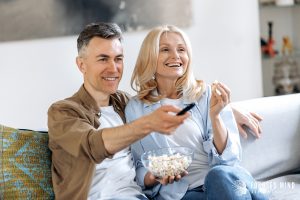 A happy couple sit together while watching a movie with popcorn at home. This could symbolize the bonds cultivated from working with a therapist in Columbus Ohio. Search for ADD and relationships today for support.