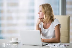 A woman stares off into the distance while sitting at a laptop desk. Learn how a Columbus ADHD therapist can offer support in gaining ADHD productivity hacks. Search for a columbus ADHD therapist for more ADHD motivation hacks in Columbus, OH today. 