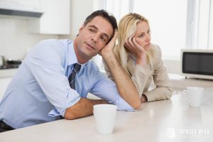 A frustrated couple sits silently at a kitchen table, illustrating the emotional disconnect and communication challenges that can result from an ADHD shutdown and rejection sensitive dysphoria.