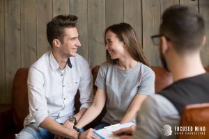 A couple smiles and holds hands during a counseling session, showing the positive outcomes of ADHD counseling and improved emotional connection through couples therapy.