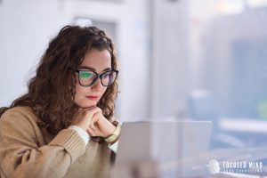 Woman with curly hair and glasses concentrating at her desk, searching online for ADHD testing in Columbus Ohio and support from an adult ADHD therapist in Ohio.
