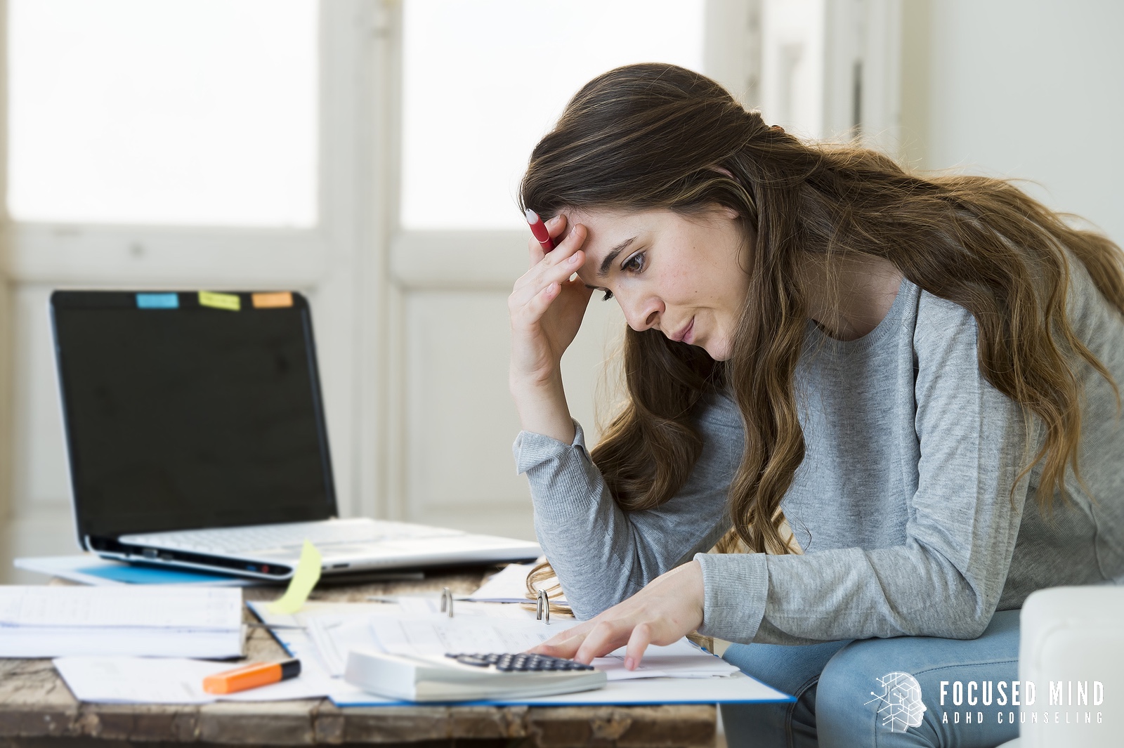 A woman sits at a cluttered desk with her hand on her forehead, overwhelmed by tasks—symbolizing the mental strain of ADHD and overthinking. This image reflects the emotional fatigue often discussed in ADHD treatment in Columbus, Ohio, especially when exploring what is RSD and how it impacts executive function.