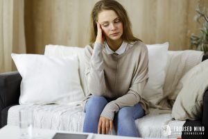 tired woman | adhd and overthinking | adhd symptoms columbus, oh | adhd therapist in columbus, oh | columbus, oh Tired woman sitting on a couch with her head in her hand – Depicting struggles tied to ADHD symptoms in Columbus, OH and how an ADHD therapist in Columbus, OH can help adults overcome overthinking.