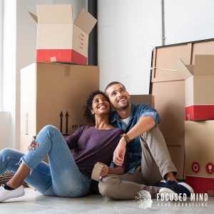 A happy couple sits on the floor surrounded by moving boxes, representing progress made through couples therapy in Columbus, OH, guidance from an ADHD couples therapist in Columbus, OH, and support for ADHD in adults Ohio.