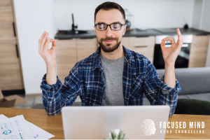 A man wearing glasses sits calmly in front of his laptop, practicing a mindfulness pose as he works on emotional balance. This peaceful moment represents how techniques learned in emotional regulation therapy in Columbus, OH can help adults manage ADHD and emotional regulation challenges. He could also be working with an ADHD therapist for adults near me to strengthen focus and reduce stress.