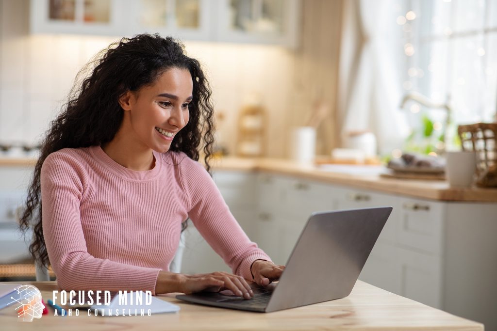 A woman smiles while working on her laptop in a bright kitchen setting. Are you wondering how an ADHD diagnosis could clarify the focus challenges you face? ADHD online testing in Cincinnati, OH, can offer insights to support better daily structure and confidence.