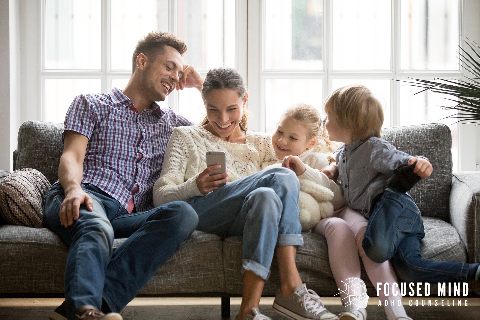 Image of a happy family sitting on a couch together. Parenting with adult ADHD can be difficult to navigate without help. Online ADHD testing in Cincinnati, OH, can be the first step toward getting the support you need.