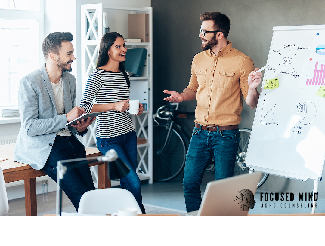 Three coworkers laugh and collaborate around a whiteboard. Rejection sensitive dysphoria can make workplace interactions feel overwhelming, even in positive environments. An ADHD specialist in Cleveland, OH, can help you understand and manage your emotional responses.