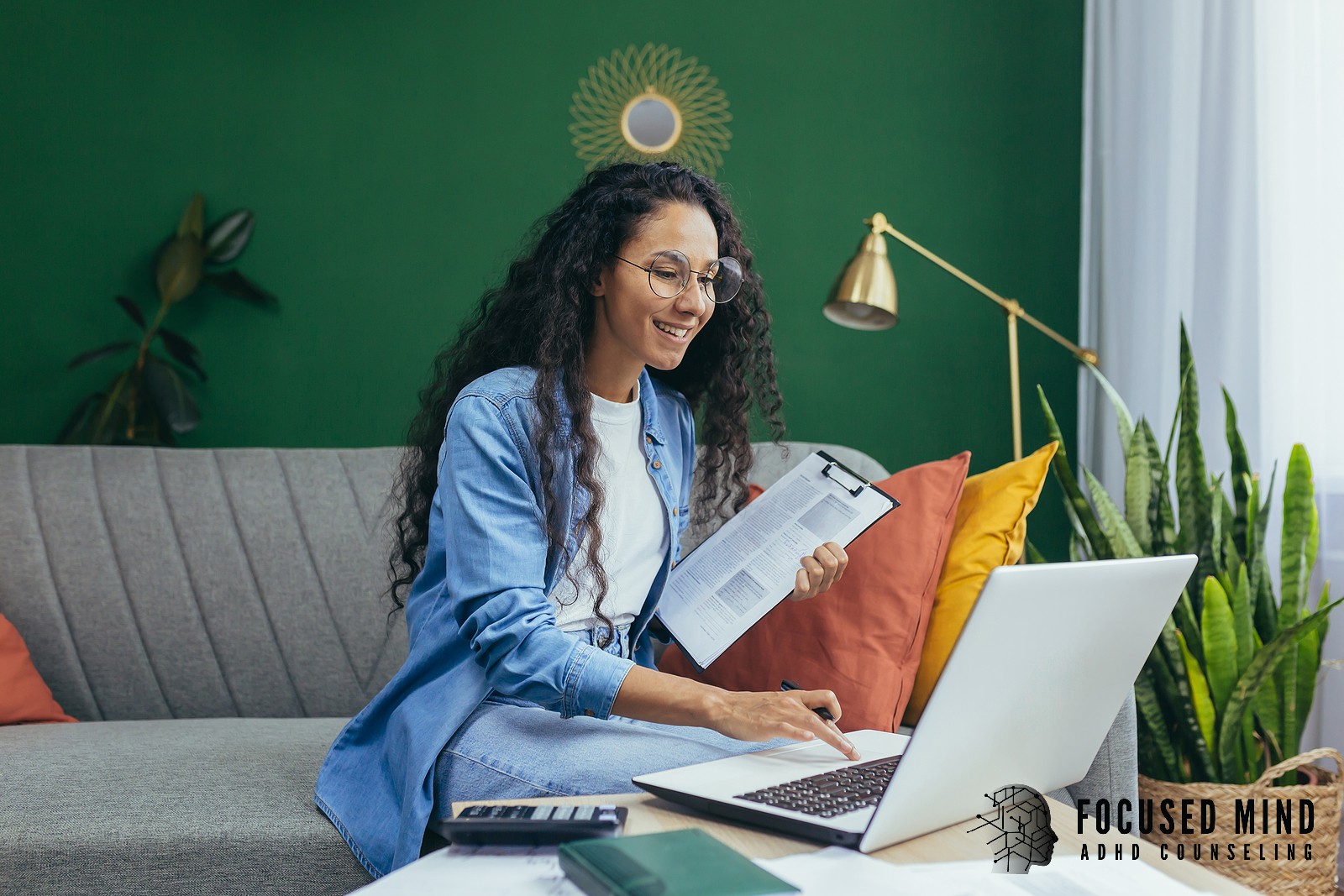 A woman smiles and holds a clipboard while working on a laptop. Productivity becomes more achievable when ADHD is properly understood and effectively managed with professional support. ADHD testing in Cincinnati, OH can help you identify the right path forward.