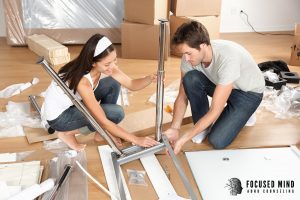 A couple sits on the floor together assembling furniture, working side by side with focus and what appears to be lighthearted cooperation. This image reflects one of the key strategies covered in ADHD therapy in Columbus, OH — sharing responsibilities based on each partner's natural strengths rather than defaulting to frustration when things don't go as planned. An ADHD counselor in Columbus, OH helps couples find this kind of collaborative rhythm in their everyday life together.