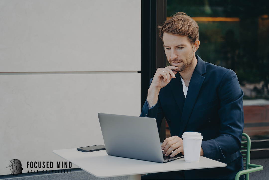 A thoughtful man in a suit rests his chin thoughtfully on his hand while working on a laptop outdoors. Could ADHD be behind the focus and concentration struggles you experience every day at work? An ADHD specialist in Cincinnati, OH, can help you find out.